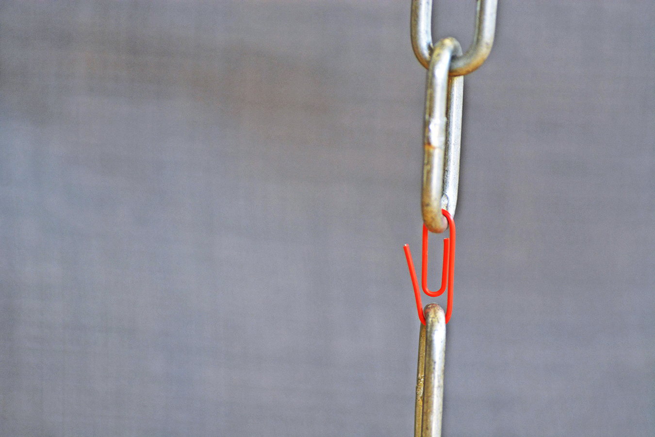 A red paperclip holds two steel chain ends together - Weakest point in chain represented by a paperclip in a normal chain - Concept for teamwork abstract illustrated